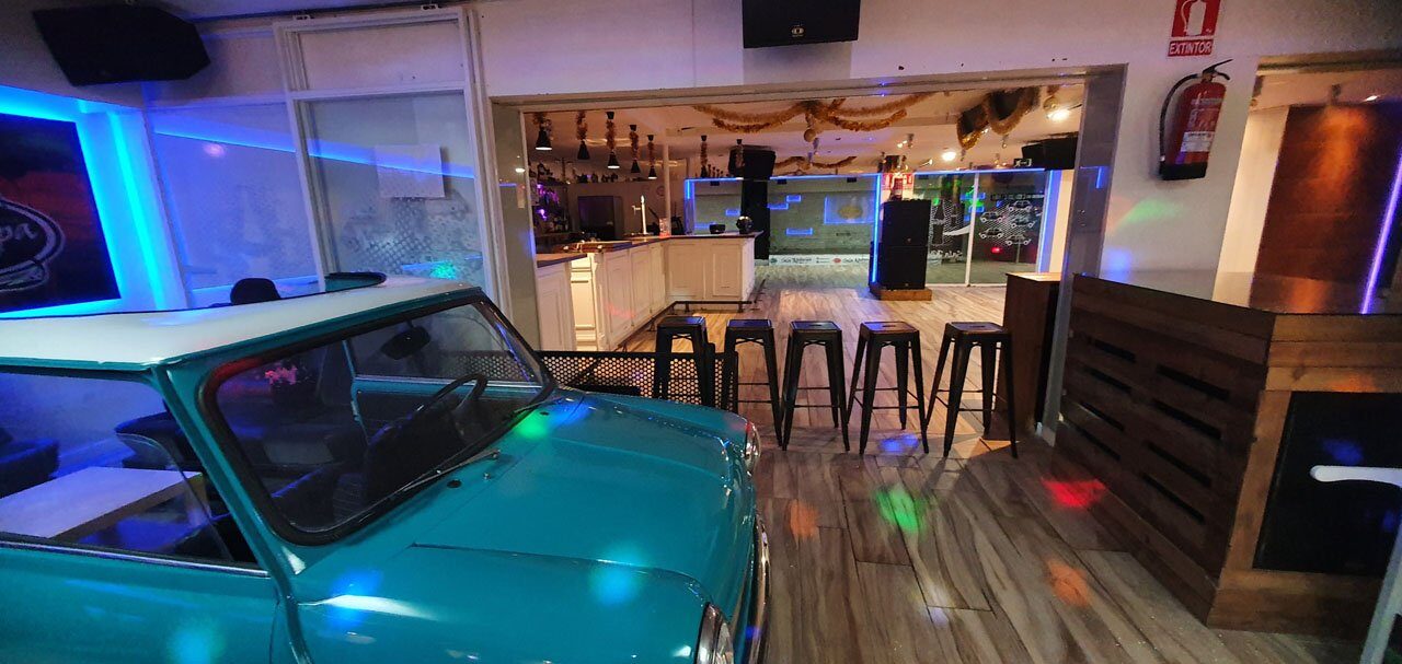 Un Mini turquesa en primer término y, al fondo, la barra con taburetes altos