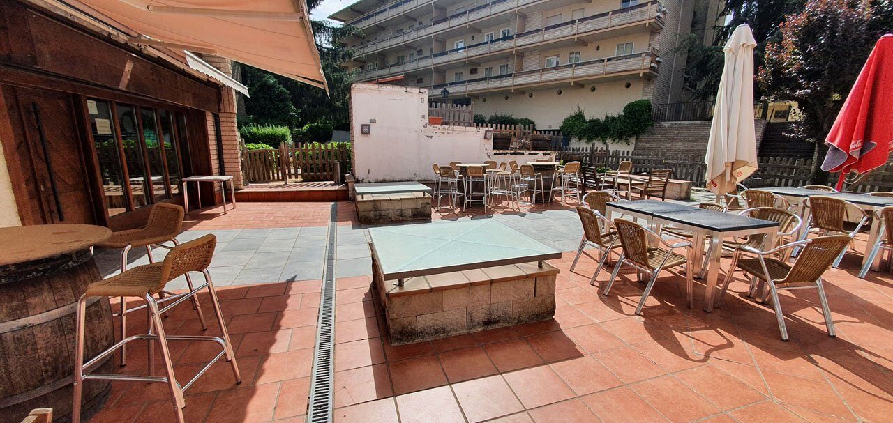 La terraza exterior con mesas, sillas y sombrillas cerradas